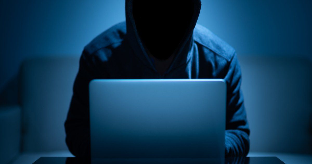 Pessoa encapuzada usando notebook, representando invasão de conta bancária