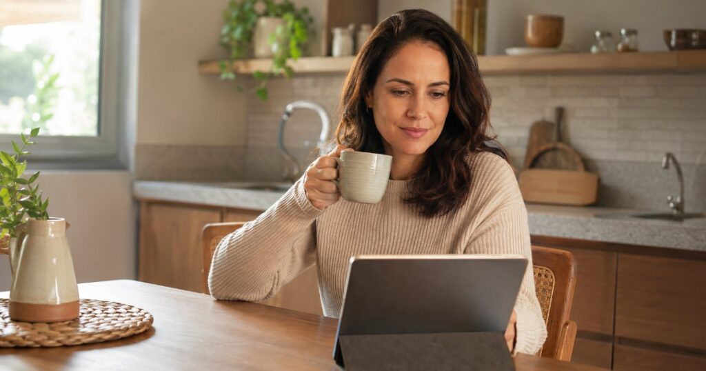 Mulher tomando café e consultando um tablet em uma cozinha aconchegante, refletindo sobre direitos do beneficiário de plano de saúde