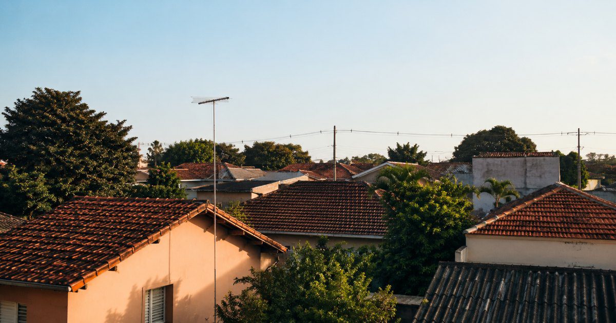 Telhados de um bairro residencial com antena e cabos aereos sob ceu claro no fim da tarde