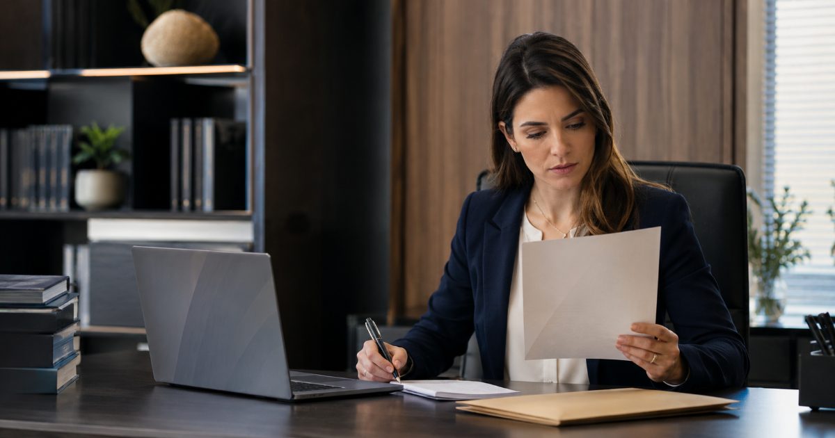 Advogada em escritório lendo com atenção um documento formal e preparando uma resposta em seu notebook